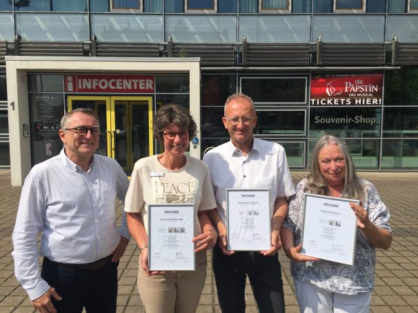 Vor dem Infocenter in Hameln präsentieren von links der HMT-Geschäftsführer Harald Wanger, Mitarbeiterin und Qualitätsbeauftragte Nicole Titz, der Leiter Hallenmanagement Oliver Meinecke und Hallen-Mitarbeiterin sowie Qualitätsbeauftragte Angela Koelman stolz die „Reisen für alle“-Urkunden, die sie für barrierefreie Angebote erhalten haben. © Hameln Marketing | Vor dem Infocenter in Hameln präsentieren von links der HMT-Geschäftsführer Harald Wanger, Mitarbeiterin und Qualitätsbeauftragte Nicole Titz, der Leiter Hallenmanagement Oliver Meinecke und Hallen-Mitarbeiterin sowie Qualitätsbeauftragte Angela Koelman stolz die „Reisen für alle“-Urkunden, die sie für barrierefreie Angebote erhalten haben. © Hameln Marketing